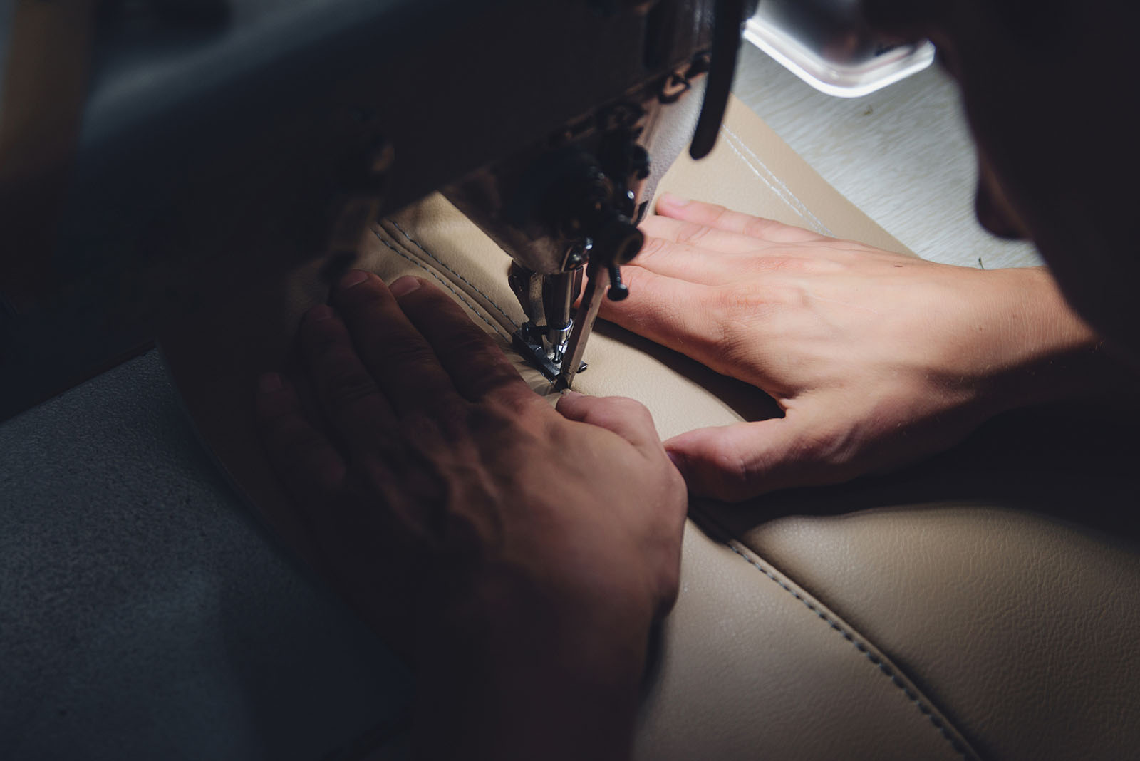 A trimmer guiding pale leather through an industrial sewing machine
